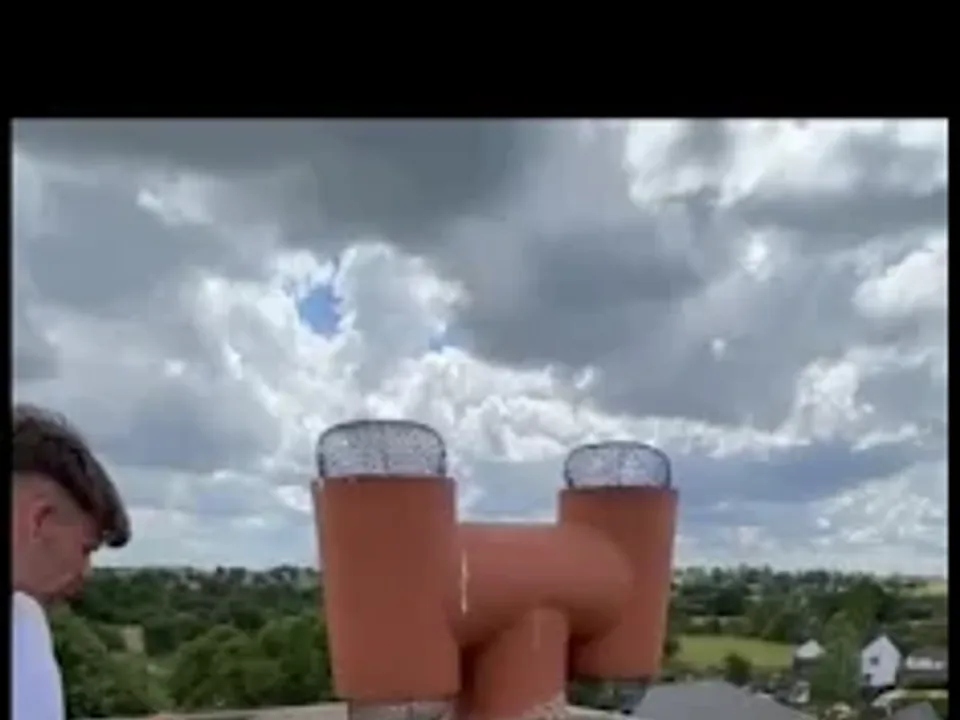 A roofer beside a rebuilt red brick chimney stack