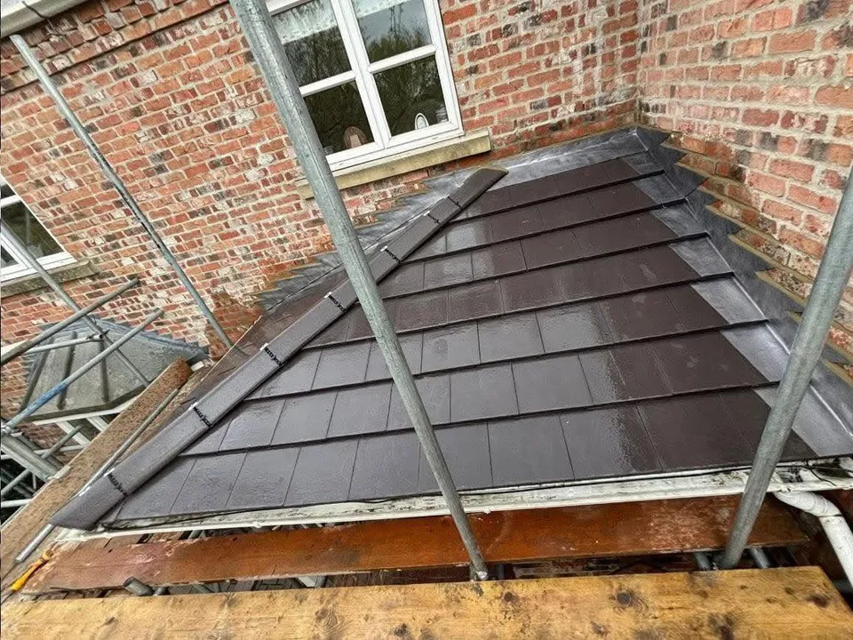 New grey roof tiles being laid during a re-roof beside red brickwork