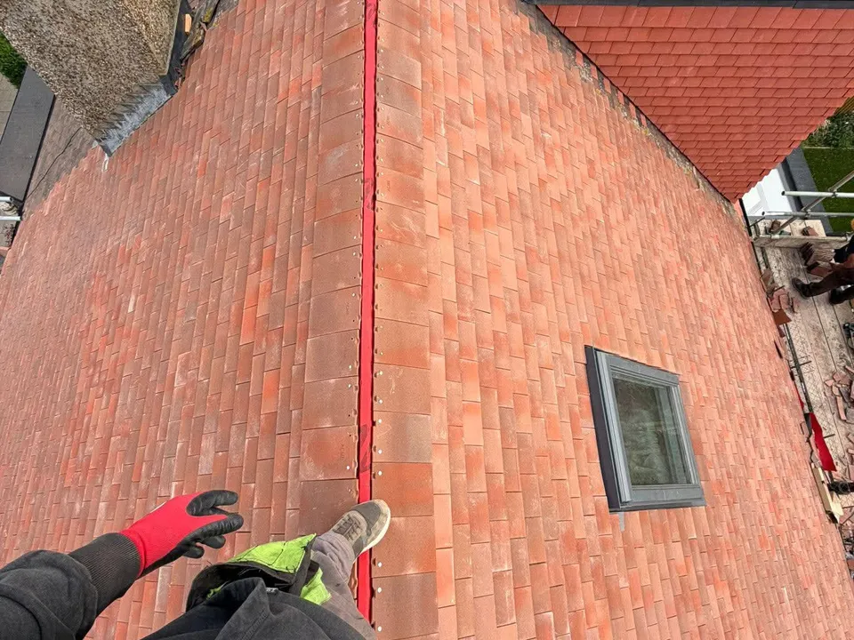 A roofer working with a trowel beside a rooflight on a red tiled roof