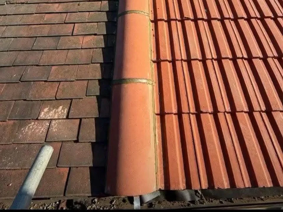 Weathered orange tiles beside fresh grey tiles on a part-finished roof